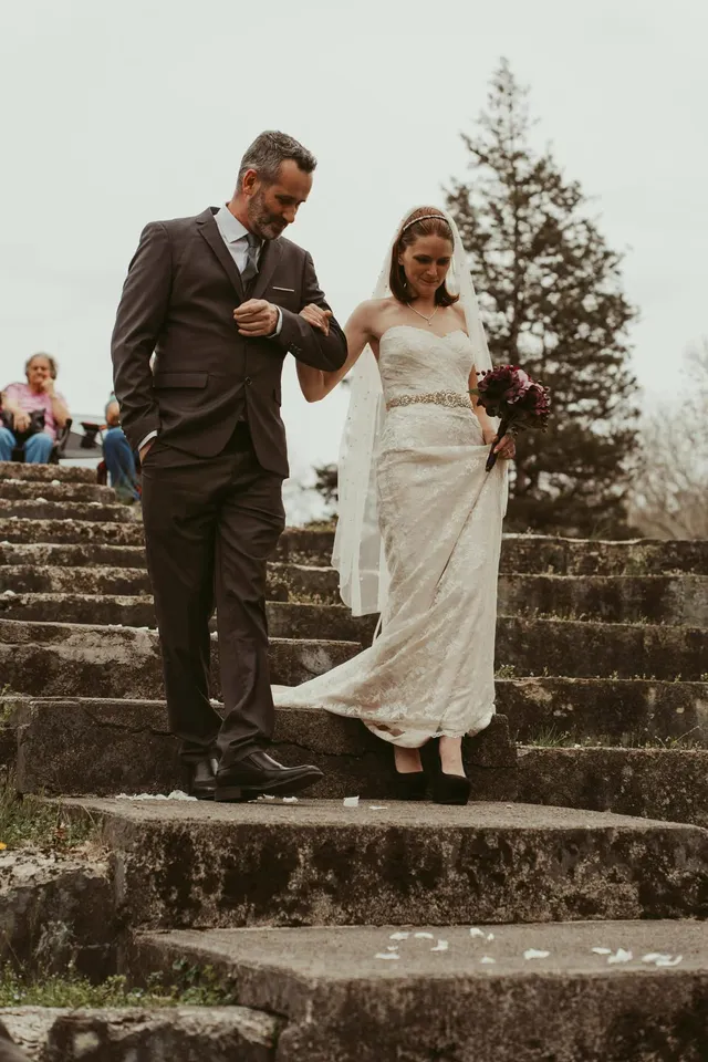 A bride and a man in a suit walking arm in arm down outdoor stone steps.