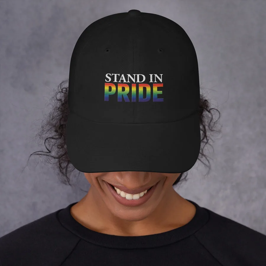 A person wearing a black cap embroidered with the rainbow Stand In Pride logo.
